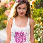 Woman wearing a Grateful Heart racerback women’s Thanksgiving tank top styled outdoors in a bright floral garden setting